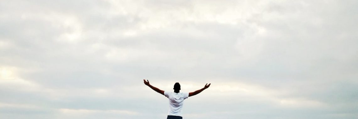 man raising hands standing near seashore during daytime