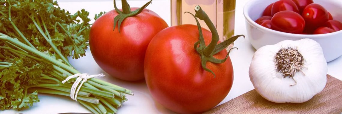 Fresh ingredients for healthy cooking featuring tomatoes, garlic, and herbs on a cutting board.